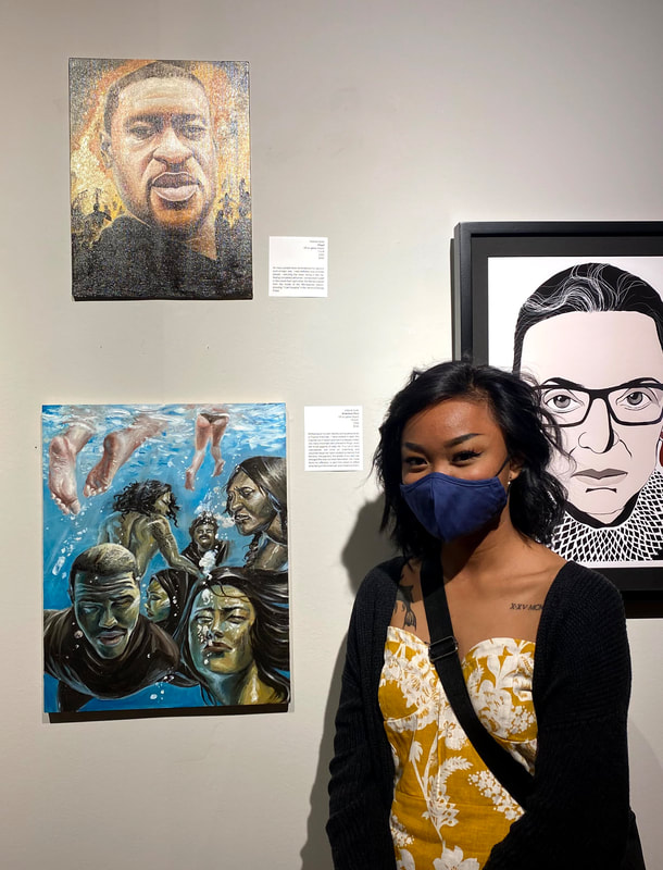 Image Description 1: Victoria is masked, standing in front of two of her paintings at an art gallery. Her first painting depicts George Floyd, and her second painting depicts people of color swimming deep in a pool underwater, while white and Caucasian people swim above water.